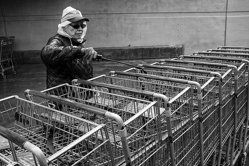 Worker at Costco in Carlsbad, CA spraying disinfect on push carts before customers can use them during the COVID-19 lock down. Photograph by James D. Phenicie, 2020.